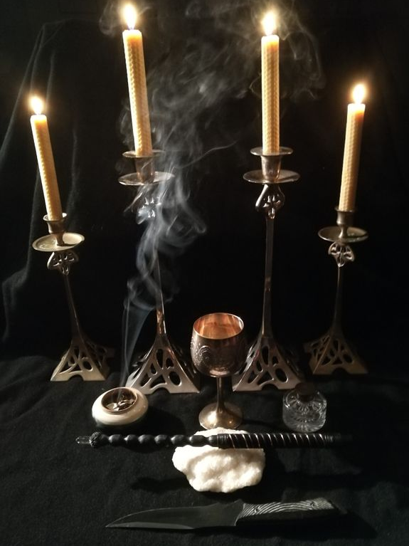 A ritual altar setup with four lit beeswax candles in metal holders, an incense burner, a chalice, a ceremonial dagger, and a wand